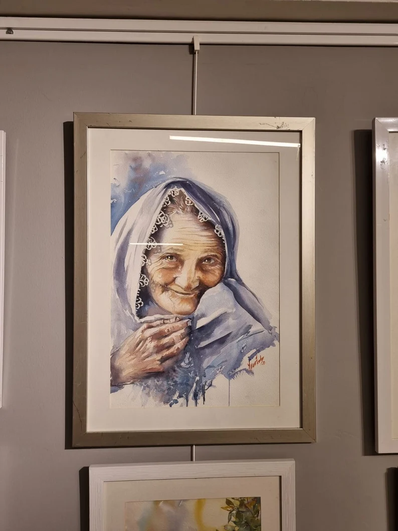 Aynur Akalın imzalı, iğne oyalı başörtülü gülen yaşlı kadın portresi, figüratif suluboya tablo çalışması.